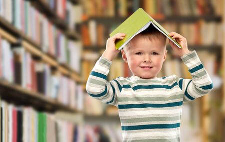 smiling boy with book on head over libraryの写真素材