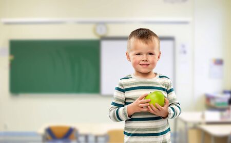 smiling boy holding green apple at schoolの写真素材