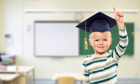 boy in mortar board pointing finger up at school