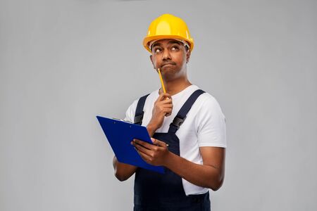 profession, construction and building - thinking indian worker or builder in helmet with clipboard...
