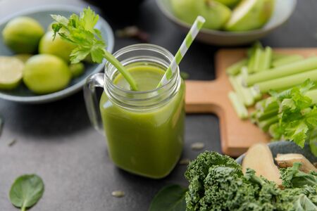 healthy eating, food and vegetarian diet concept - close up of glass mug of fresh green juice or smoothie with paper straw, fruits and vegetables on slate stone backgroundの写真素材