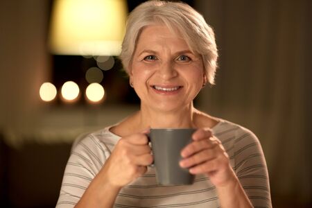old age, drink and people concept - happy smiling senior woman with cup of tea or coffee at home at...