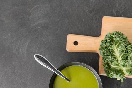 vegetable, food and culinary concept - kale cabbage cream soup in ceramic bowl with spoon on slate...