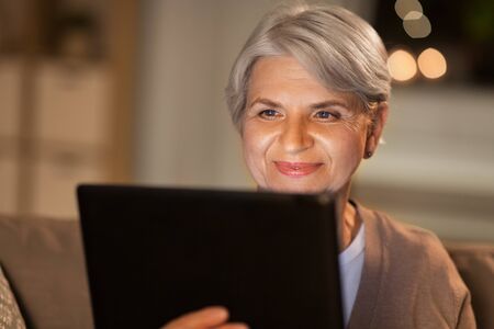 happy senior woman with tablet pc at home at night