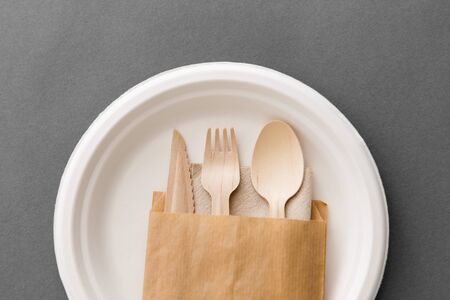 cutlery, recycling and eco friendly concept - set of wooden spoon, fork and knife on paper plate on grey backgroundの写真素材