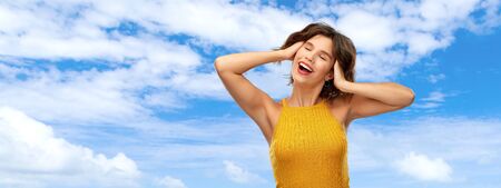 happy laughing young woman in yellow top over skyの写真素材