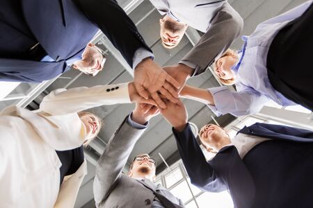 corporate, people and teamwork concept - happy business team stacking hands at office from below