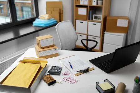 delivery, mail service and shipment concept - laptop, clipboard, parcel boxes and packing stuff on...