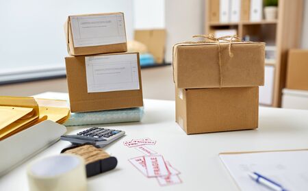 delivery, mail service and shipment concept - parcel boxes with postal forms on table at post office