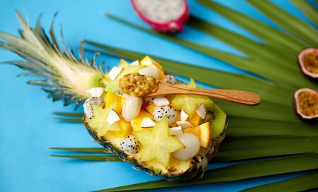 food, summer and healthy eating concept - mix of different exotic fruits in pineapple with wooden spoon on green fan palm leaf and blue backgroundの写真素材