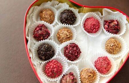sweets, confectionery and food concept - candies in red heart shaped chocolate box on brown...