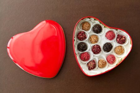 sweets, confectionery and food concept - candies in red heart shaped chocolate box on brown...