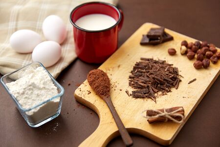confectionery and culinary concept - chocolate, cocoa powder, hazelnuts with milk, eggs and flour on brown backgroundの写真素材