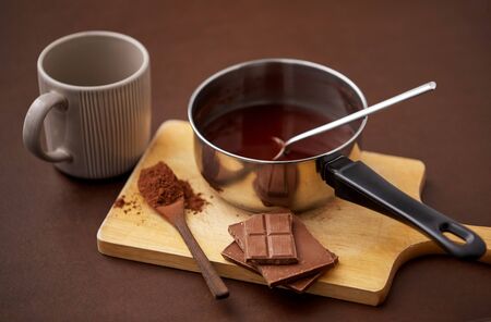 sweets, confectionery and culinary concept - pot with melted hot chocolate, cocoa powder in spoon,...