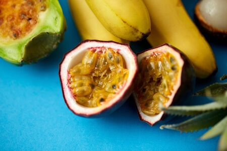 food and eating concept - close up of cut passion fruit with other exotic fruits on blue background