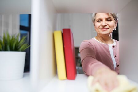 happy senior woman with cloth dusting rack at home