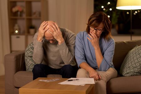 unhappy senior couple with bills and money at home