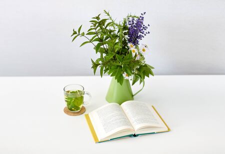 eco and organic concept - cup of green herbal tea, book and flowers in jug on tableの写真素材