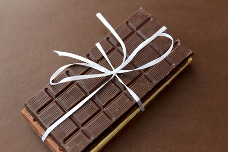 sweets, confectionery and food concept - different kinds of chocolate tied with white ribbon on brown backgroundの写真素材
