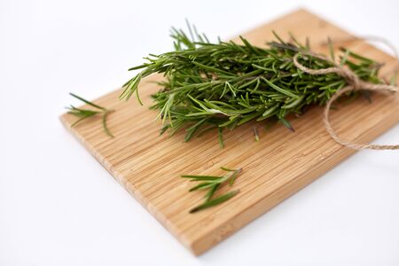 greens, culinary and ethnoscience concept - bunch of rosemary on wooden cutting boardの写真素材