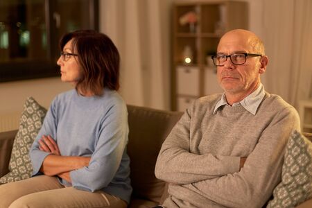 relationships difficulties, problem and people concept - unhappy senior couple sitting on sofa at...
