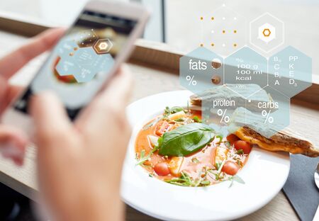 food, eating, technology, culinary and people concept - woman hands with gazpacho soup photo on smartphone screen and nutritional value chart at restaurantの写真素材