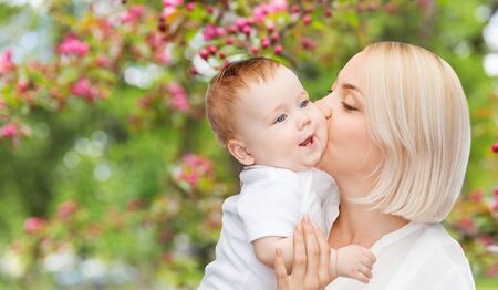 close up of happy mother kissing baby over gardenの写真素材