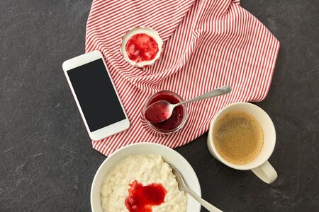 porridge with jam, spoon, coffee and phoneの写真素材