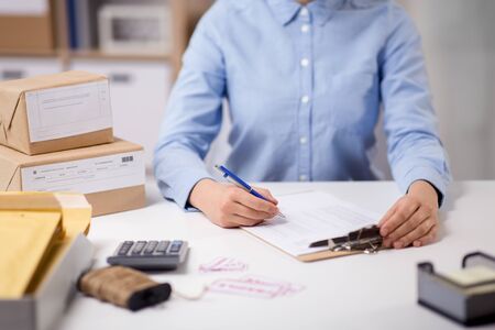 delivery, mail service, people and shipment concept - close up of woman with clipboard filling checklist at post officeの写真素材