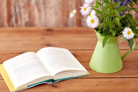 book and flowers in jug on wooden table