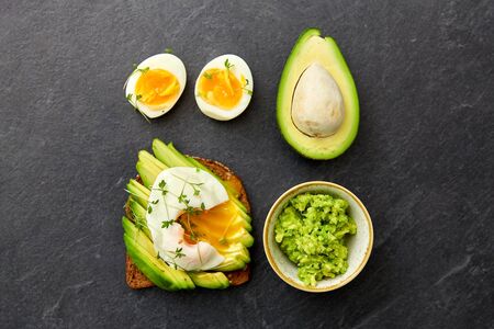 food, eating and breakfast concept - toast bread with sliced avocado, pouched egg and greens on...