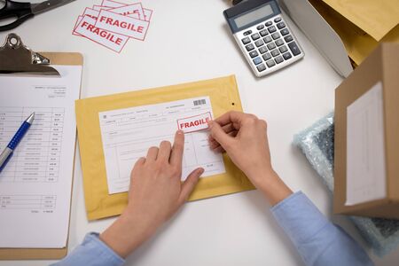 hands sticking fragile marks to parcel in envelope