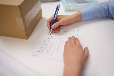 delivery, mail service, people and shipment concept - close up of woman filling postal form at...