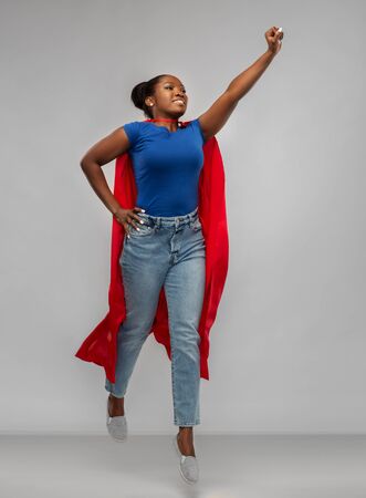 happy african american woman in red superhero capeの写真素材