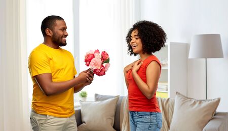 holiday, greeting and people concept - happy african american couple with bunch of flowers over home backgroundの写真素材