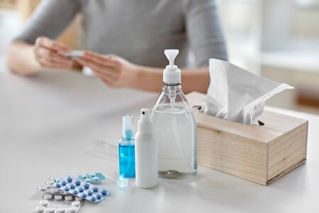 medicines and sick woman with thermometer at home
