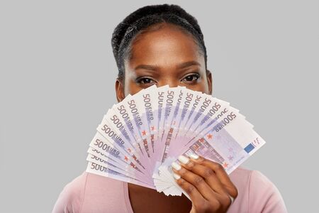 finance, currency and people concept - african american young woman holding euro money banknotes...