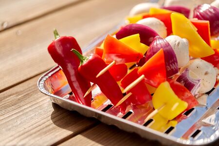 cooking, barbecue and food concept - close up of vegetables with champignons on skewers stacked on disposable foil grill on wooden tableの写真素材