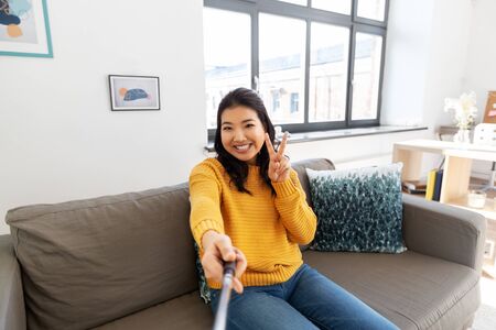 woman taking selfie and showing peace at homeの写真素材