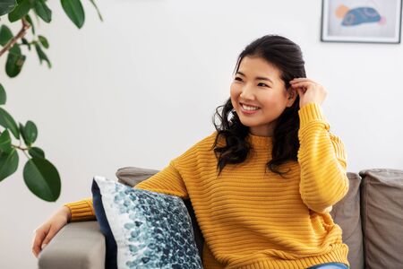 smiling asian young woman sitting on sofa at home