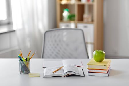 books, apple and school supplies on table at homeの写真素材