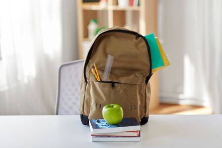 school backpack with books and apple on tableの写真素材