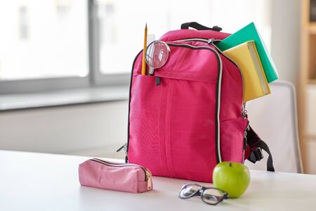 pink backpack, apple and school supplies on table