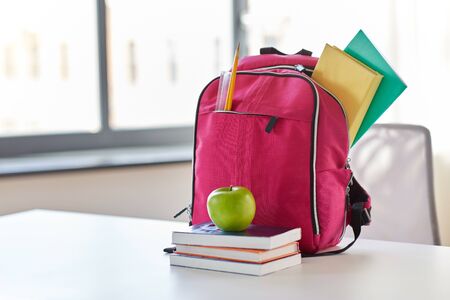 pink backpack, apple and school supplies on tableの写真素材
