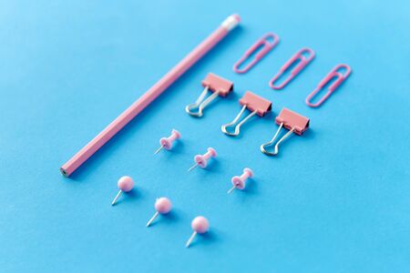 pink pencil, pins and clips on blue background