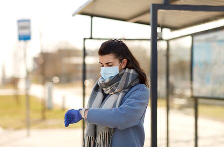 woman in mask looking at wristwatch at bus stopの写真素材