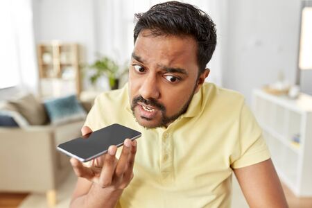 angry man recording voice on smartphone at home