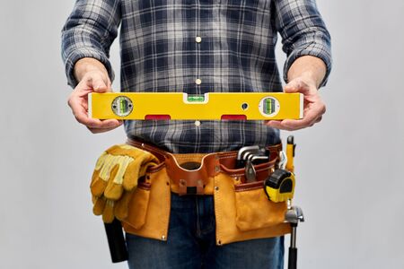 repair, construction and building - male worker or builder with level and working tools on belt over grey backgroundの写真素材