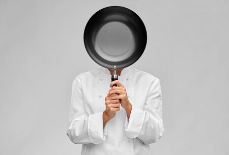 female chef covering her face with frying panの写真素材