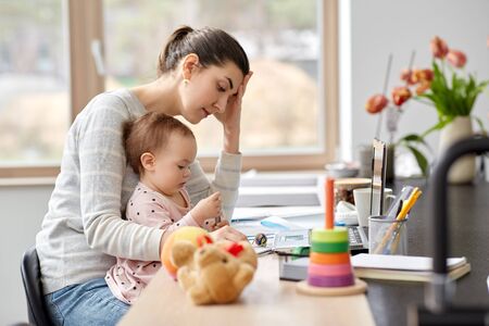 tired mother with baby working at home officeの写真素材